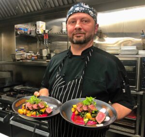 Chef standing in a kitchen with two plates of food